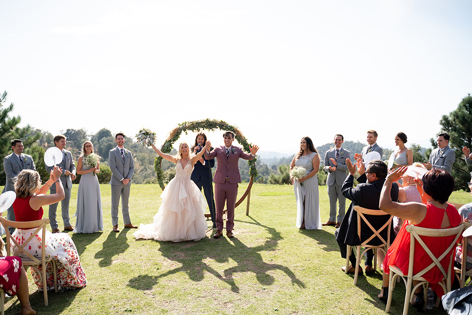  bride in a white ballgown with a deep-v neckline and crystal embellishments and the groom in a rose pink suit with a navy floral neck tie 