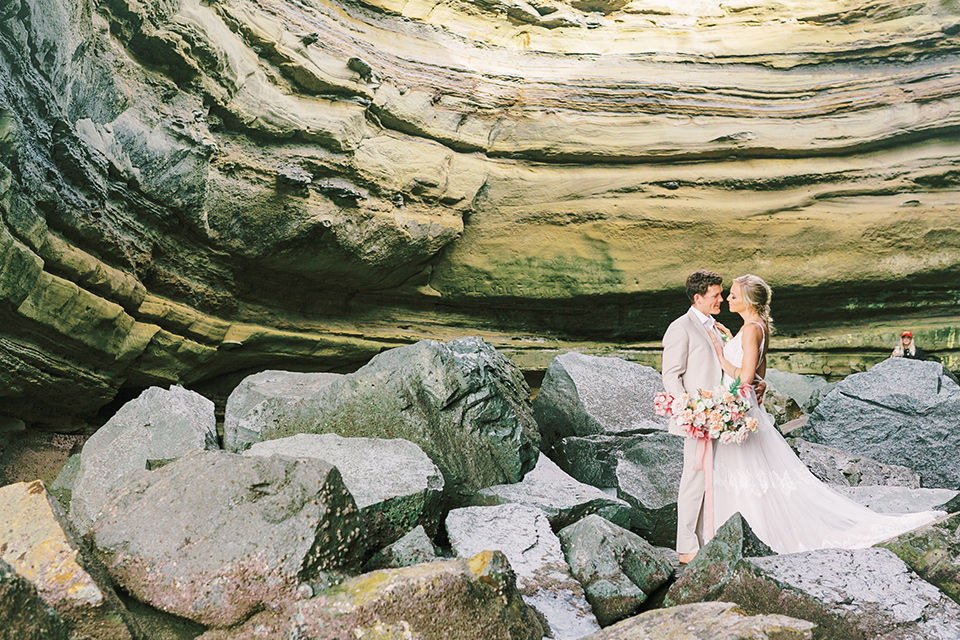  bride in a flowing blush and white gown with a silk style top and the groom in a tan suit with no tie and light brown shoes 