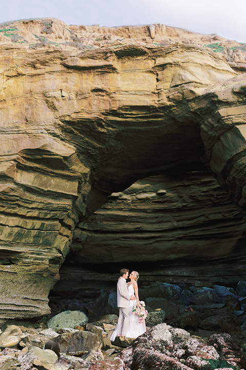  bride in a flowing blush and white gown with a silk style top and the groom in a tan suit with no tie and light brown shoes 