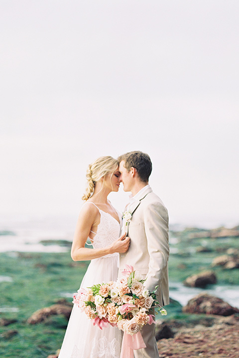  bride in a flowing blush and white gown with a silk style top and the groom in a tan suit with no tie and light brown shoes 