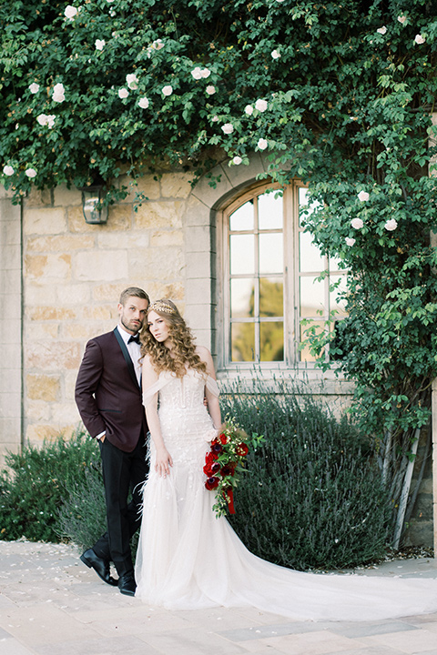  bride in a lace formfitting gown with an off the shoulder detail and the groom in a burgundy tux and black bow tie