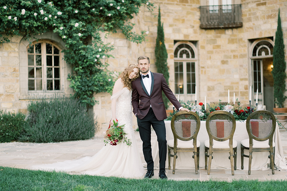 bride in a lace formfitting gown with an off the shoulder detail and the groom in a burgundy tux and black bow tie 