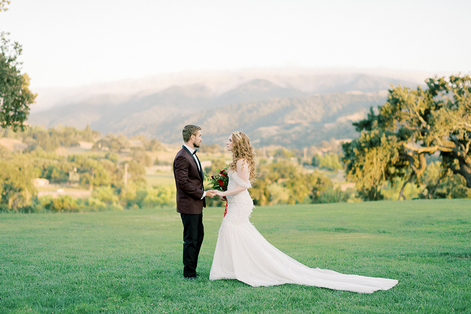  bride in a lace formfitting gown with an off the shoulder detail and the groom in a burgundy tux and black bow tie 