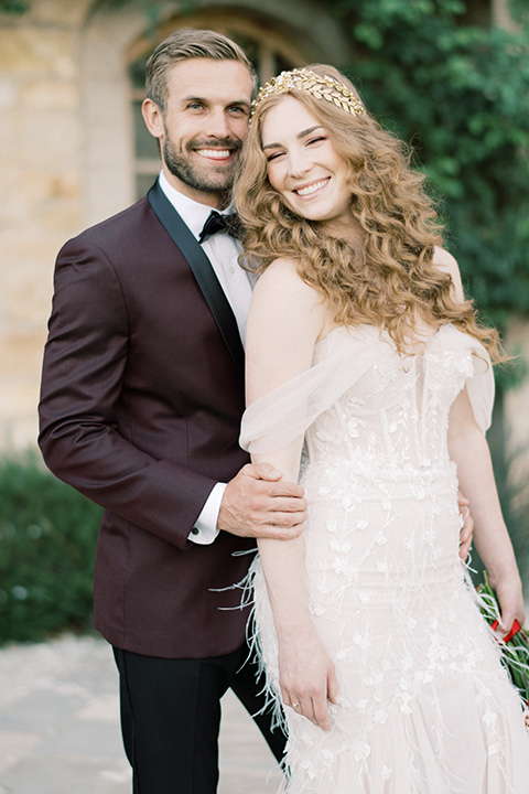  bride in a lace formfitting gown with an off the shoulder detail and the groom in a burgundy tux and black bow tie