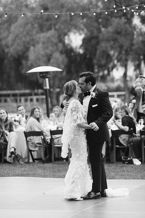  bride in a white gown with floral appliques and trumpet sleeves, the groom in a black tuxedo with black tie accessories 