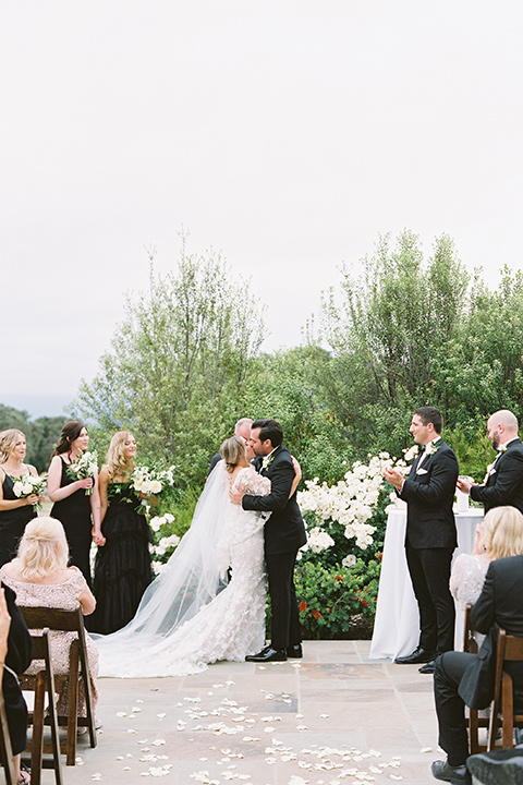  bride in a white gown with floral appliques and trumpet sleeves, the groom in a black tuxedo with black tie accessories 