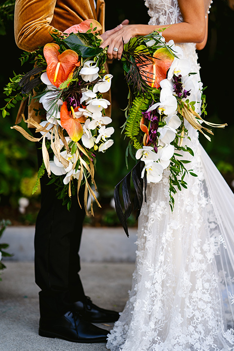  bride in a formfitting white lace gown with a sweetheart neckline and bold bouquet and the groom in a gold velvet tuxedo with black pants and black bow tie 