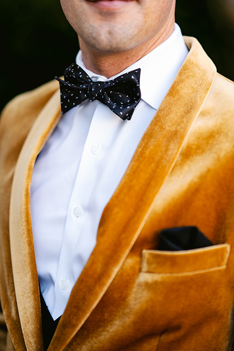 the groom in a gold velvet tuxedo with black pants and black bow tie