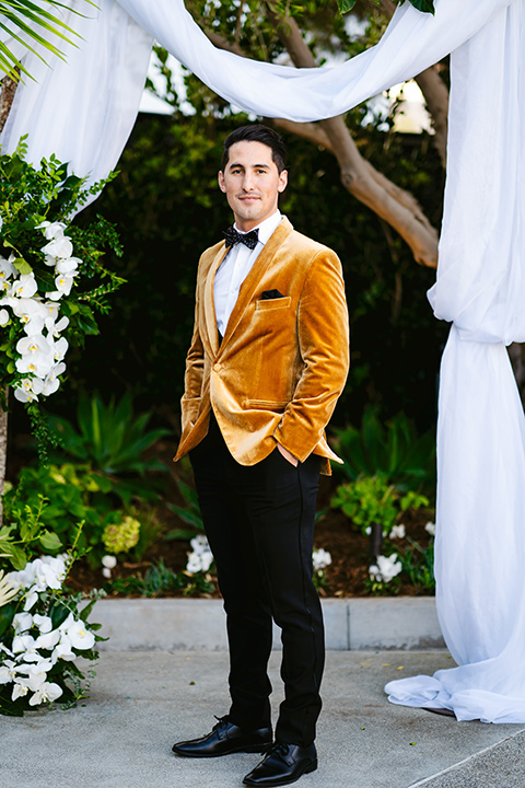 the groom in a gold velvet tuxedo with black pants and black bow tie 