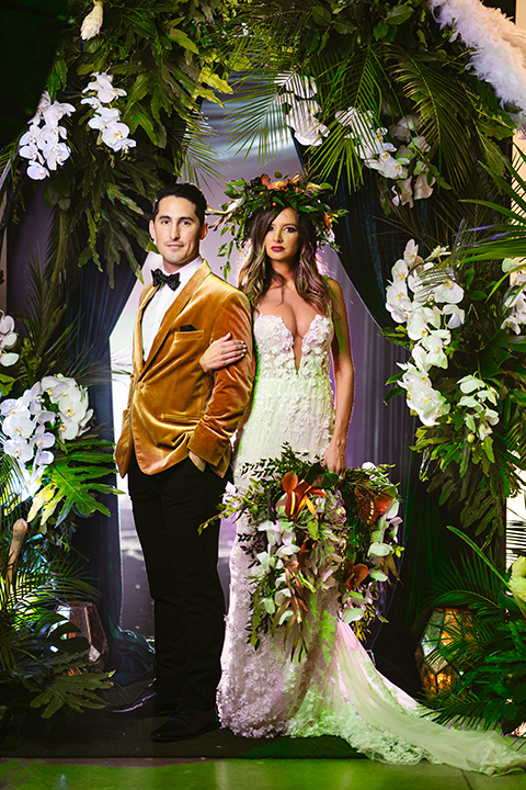  bride in a formfitting white lace gown with a sweetheart neckline and bold bouquet and the groom in a gold velvet tuxedo with black pants and black bow tie 