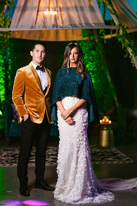  bride in a formfitting white lace gown with a sweetheart neckline and bold bouquet and the groom in a gold velvet tuxedo with black pants and black bow tie