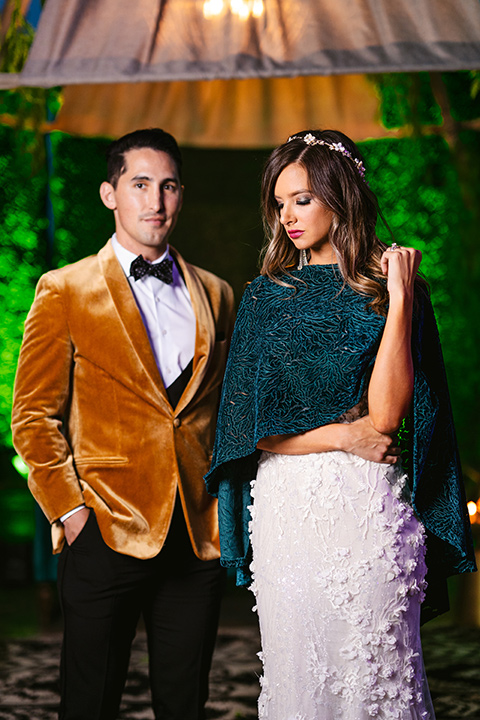  bride in a formfitting white lace gown with a sweetheart neckline and bold bouquet and the groom in a gold velvet tuxedo with black pants and black bow tie 