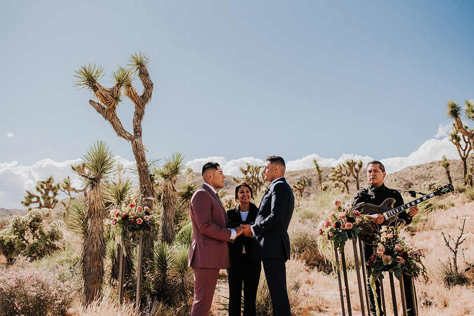  groom in a pink suit with a deep burgundy bow long tie and the other groom in a dark blue suit with a floral long tie