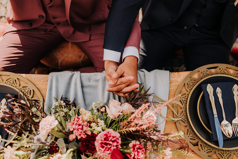  groom in a pink suit with a deep burgundy bow long tie and the other groom in a dark blue suit with a floral long tie