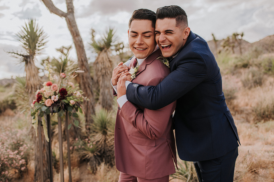 groom in a pink suit with a deep burgundy bow long tie and the other groom in a dark blue suit with a floral long tie