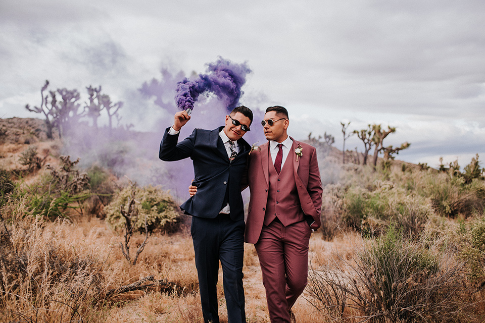  groom in a pink suit with a deep burgundy bow long tie and the other groom in a dark blue suit with a floral long tie