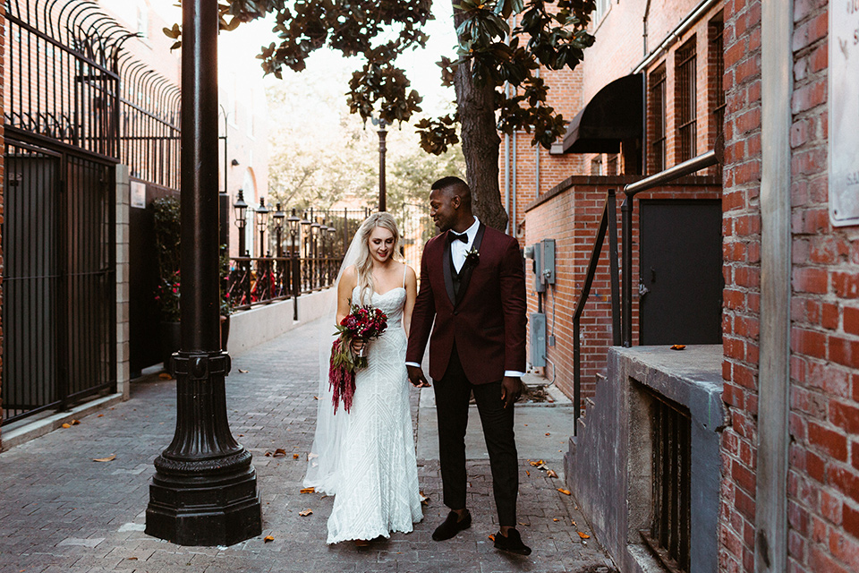 bride in a formfitting lace white gown with thin straps, and the groom in a burgundy tuxedo with a black bow tie.