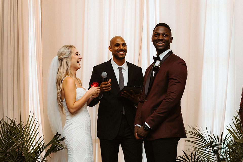 bride in a formfitting lace white gown with thin straps, and the groom in a burgundy tuxedo with a black bow tie.