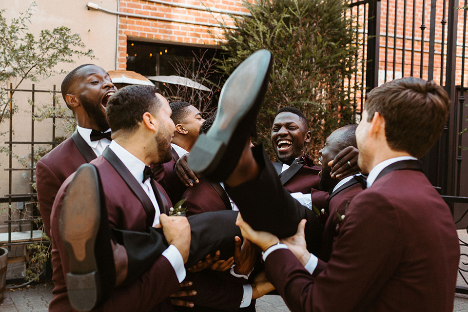  the groom in a burgundy tuxedo with a black bow tie and the groomsmen in burgundy tuxedos