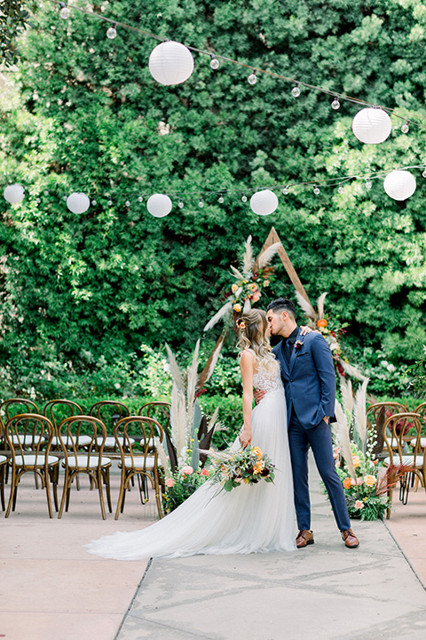 bride in a lace formfitting gown with a high neckline and the groom in a cobalt blue suit with a black shirt and blue long tie