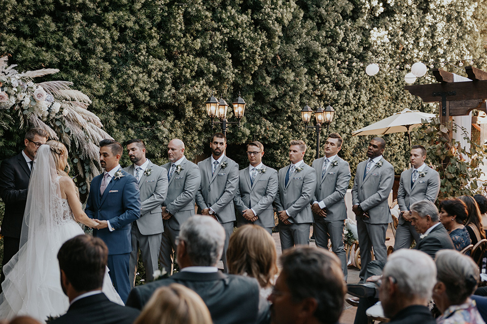 bride in a white ballgown and lace bodice detailing, the groom in a dark blue suit with a pink long tie and groomsmen in light pink suits with a dark blue vest 