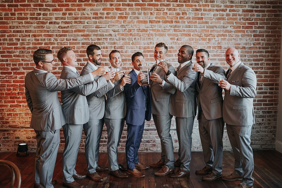  the groom in a dark blue suit with a pink long tie and groomsmen in light pink suits with a dark blue vest 