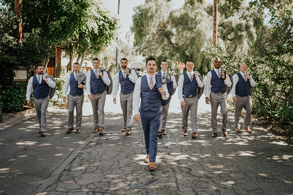  the groom in a dark blue suit with a pink long tie and groomsmen in light pink suits with a dark blue vest 