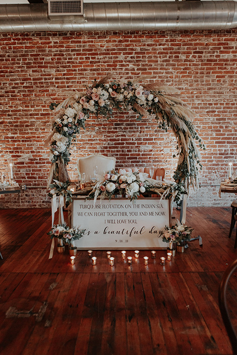 sweetheart table with white linens and a circular arch and pink florals