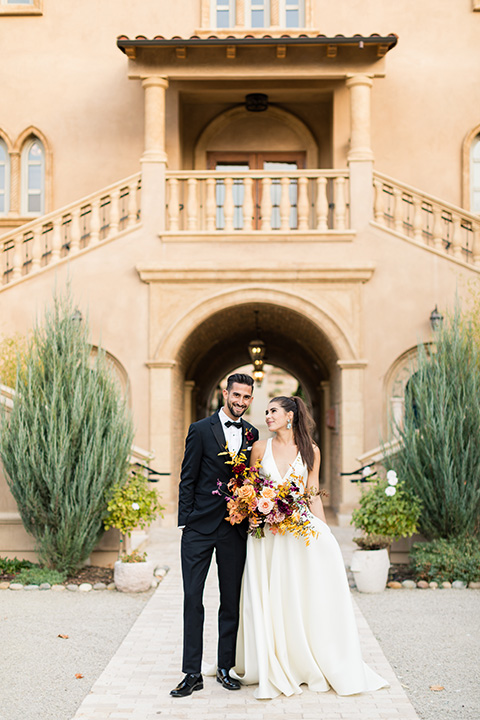 old world wedding at Allegretto Vineyard Resort – bride in a long gown with a cutout back design and the groom in black tuxedo with a black diamond bow tie at ceremony