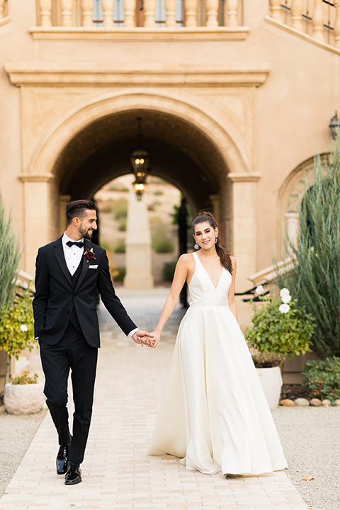  old world wedding at Allegretto Vineyard Resort – bride in a long gown with a cutout back design and the groom in black tuxedo with a black diamond bow tie at ceremony 