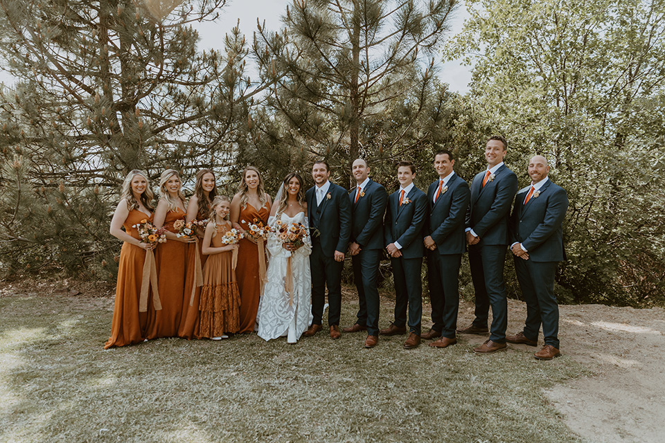  the bridesmaids in deep orange gowns, the groomsmen in navy suits, and the bride in an ivory rue de sine gown and the groom in a dark blue suit with an orange tie