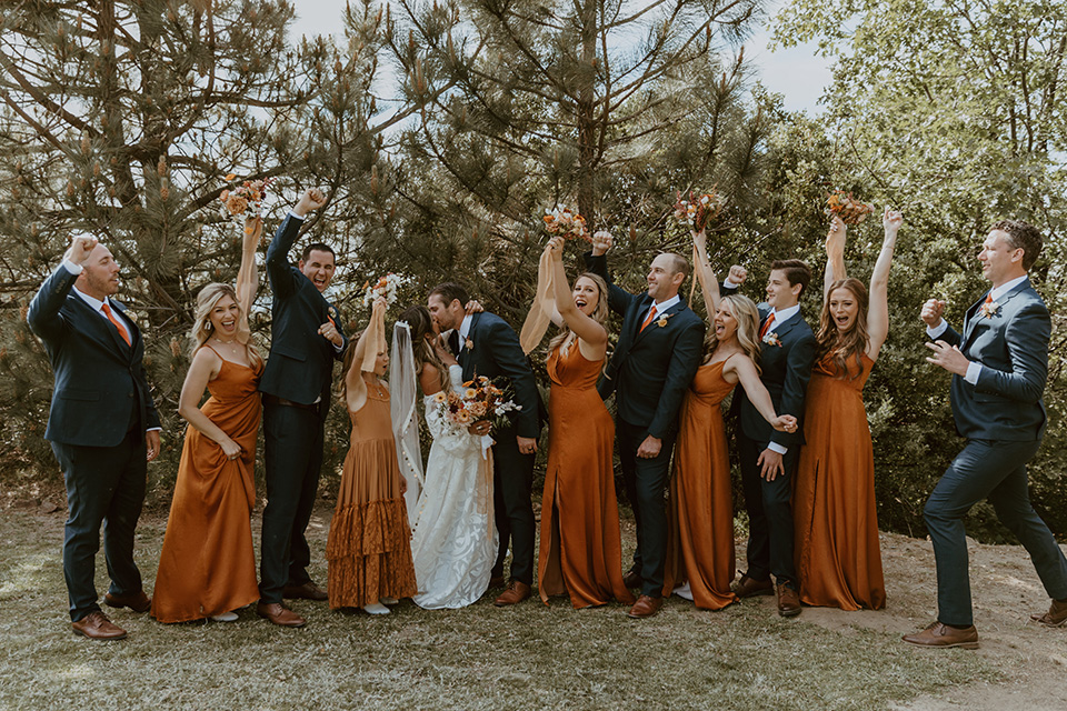  the bridesmaids in deep orange gowns, the groomsmen in navy suits, and the bride in an ivory rue de sine gown and the groom in a dark blue suit with an orange tie