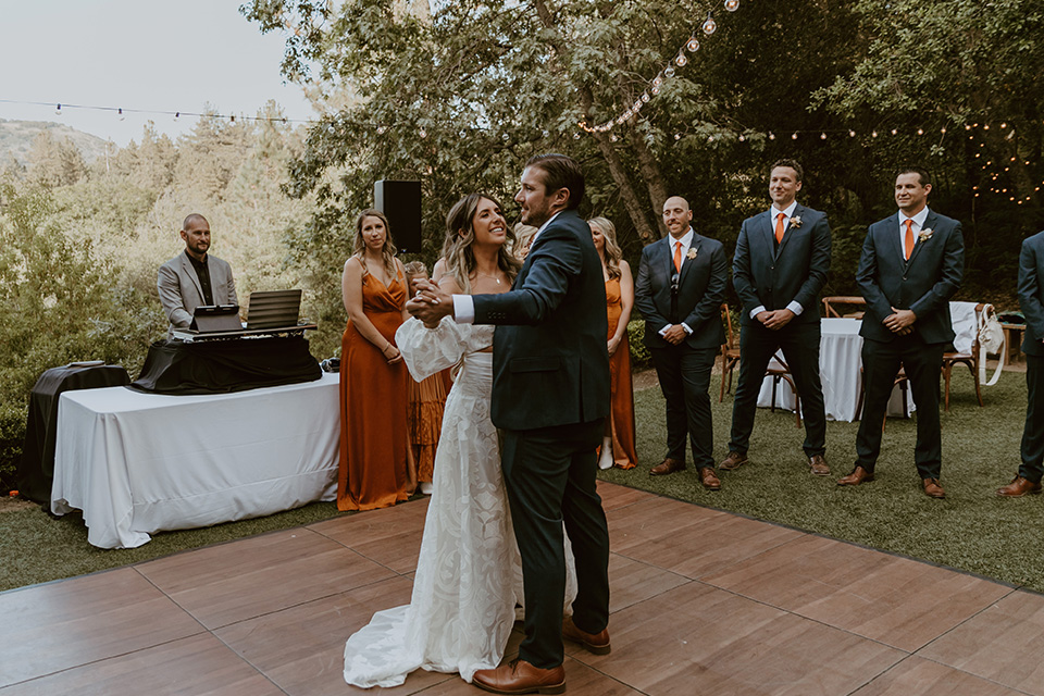  the bridesmaids in deep orange gowns, the groomsmen in navy suits, and the bride in an ivory rue de sine gown and the groom in a dark blue suit with an orange tie at the first dance