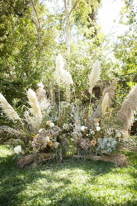  backyard bohemian elopements with the bride in a high neckline gown and the groom in a caramel suit -ceremony arch