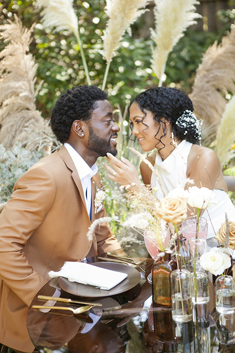  backyard bohemian elopements with the bride in a high neckline gown and the groom in a caramel suit -sitting