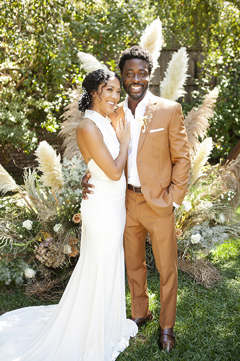  backyard bohemian elopements with the bride in a high neckline gown and the groom in a caramel suit -ceremony 