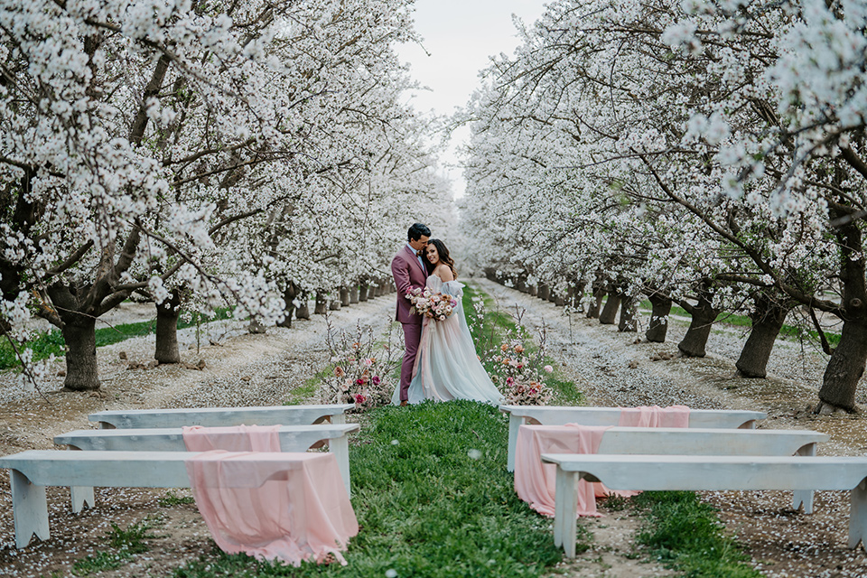  bride in a pastel pink and blue gown and the groom in a rose pink suit and gold bow tie 
