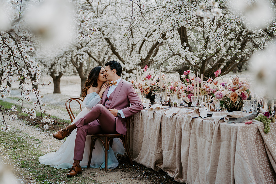  bride in a pastel pink and blue gown and the groom in a rose pink suit and gold bow tie 