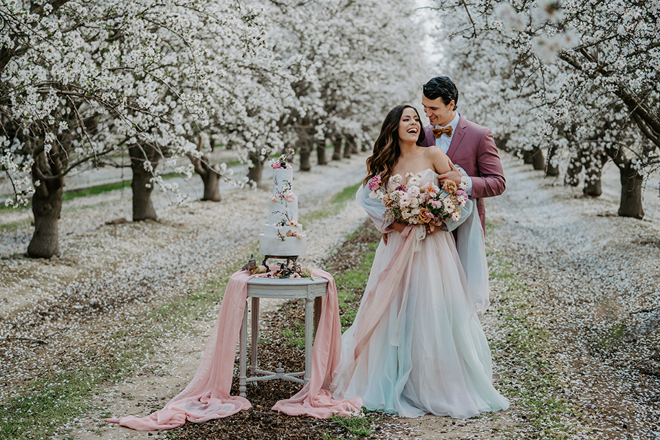  bride in a pastel pink and blue gown and the groom in a rose pink suit and gold bow tie 