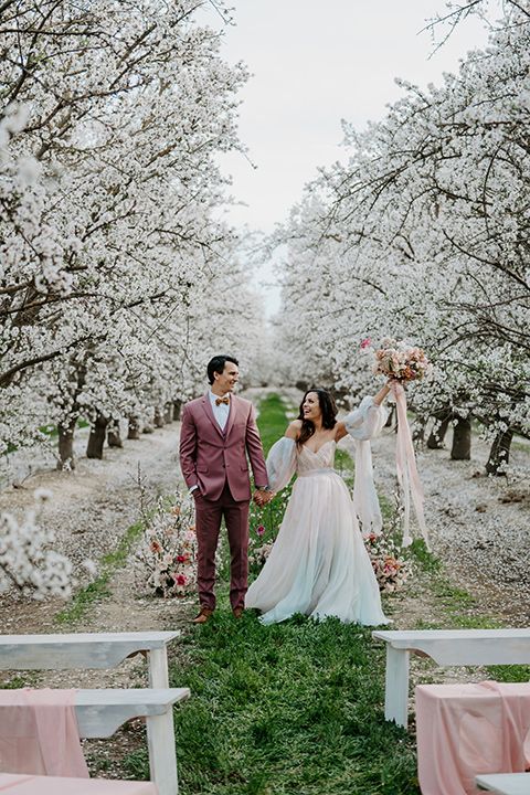   bride in a pastel pink and blue gown and the groom in a rose pink suit and gold bow tie