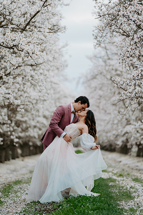   bride in a pastel pink and blue gown and the groom in a rose pink suit and gold bow tie