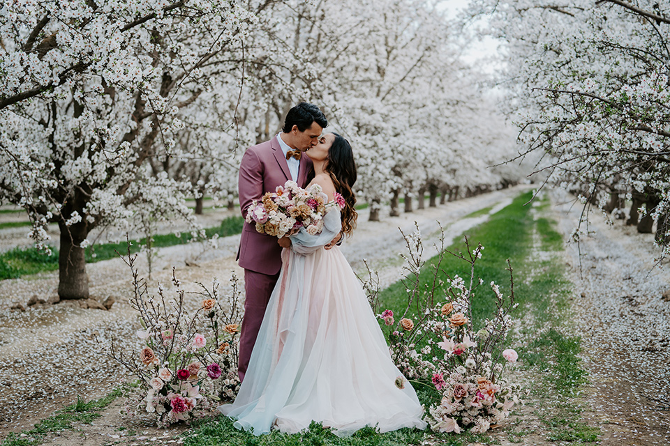  bride in a pastel pink and blue gown and the groom in a rose pink suit and gold bow tie 