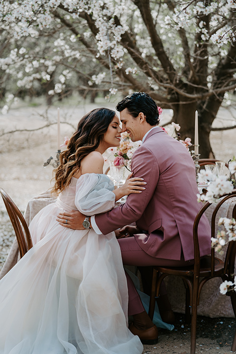  bride in a pastel pink and blue gown and the groom in a rose pink suit and gold bow tie 