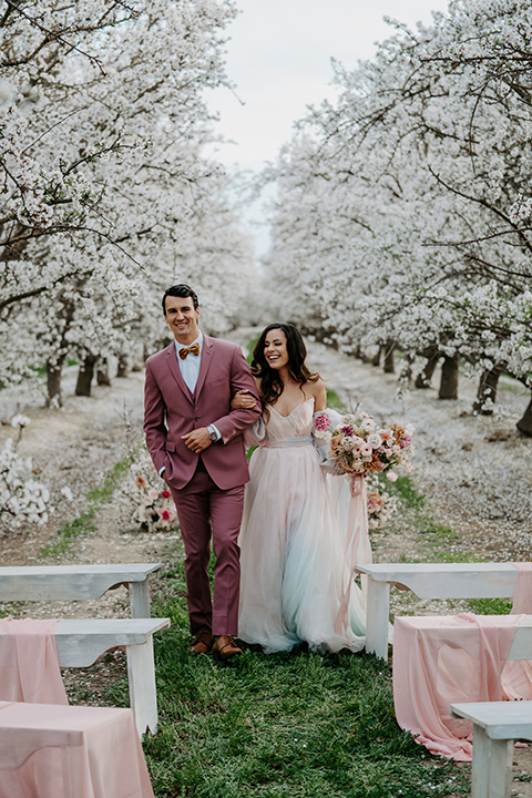  bride in a pastel pink and blue gown and the groom in a rose pink suit and gold bow tie 