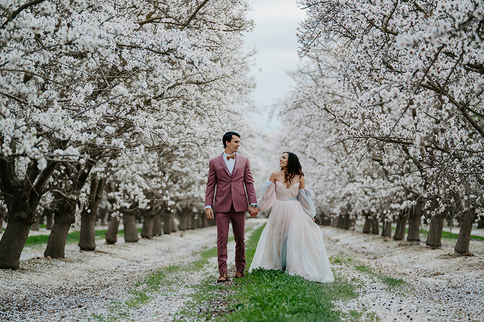  bride in a pastel pink and blue gown and the groom in a rose pink suit and gold bow tie 