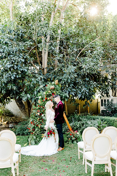  Christmas styled shoot with the groom in a burgundy velvet tuxedo and black pants  and the bride in a white long formfitting gown and long sleeves