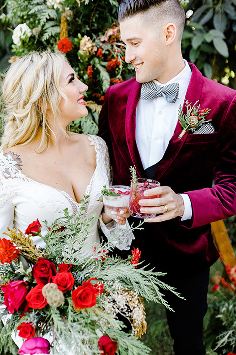  Christmas styled shoot with the groom in a burgundy velvet tuxedo and black pants  and the bride in a white long formfitting gown and long sleeves