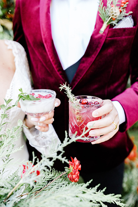  Christmas styled shoot with the groom in a burgundy velvet tuxedo and black pants  and the bride in a white long formfitting gown and long sleeves 