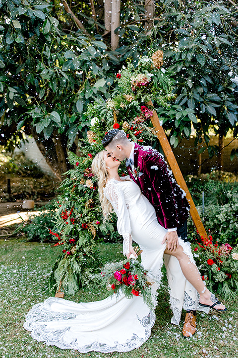  Christmas styled shoot with the groom in a burgundy velvet tuxedo and black pants  and the bride in a white long formfitting gown and long sleeves