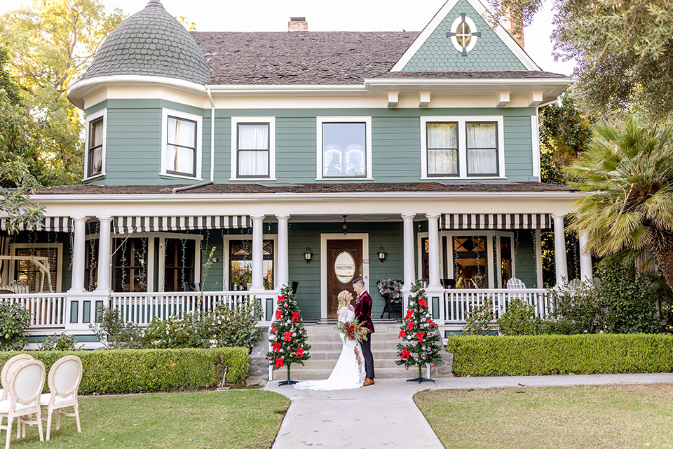  Christmas styled shoot with the groom in a burgundy velvet tuxedo and black pants  and the bride in a white long formfitting gown and long sleeves 